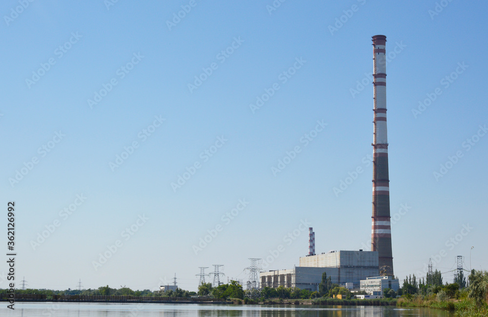 view from afar of the buildings and the pipe of the power plant. lake water and blue sky are also visible view from afar of the buildings and the pipe of the power plant. lake water and blue sky are also visible