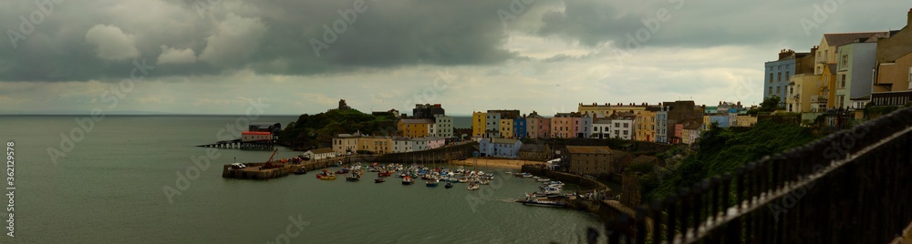 Panoramic view of Tenby, a coastal harbor town in southwest Wales. Image shows the harbor as well as the old town. The old town has traditional buildings with colorful facades.