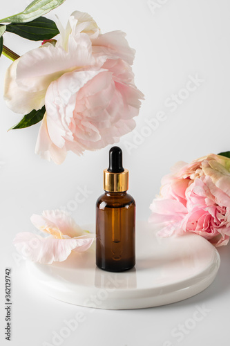 Glass brown bottle with serum and a pipette for skin care on a light background with peony flower. The concept of health and beauty. minimalism