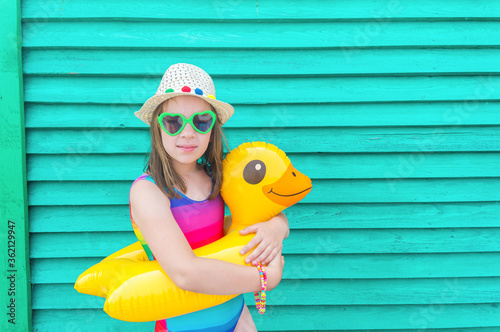 Girl with an inflatable duck. Baby in hat and glasses on a wooden background.