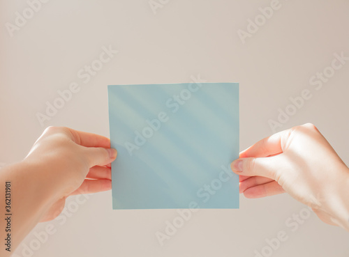  Blue square leaflet with hard shadows mock up on a white background in the hand of a young woman. School concept
