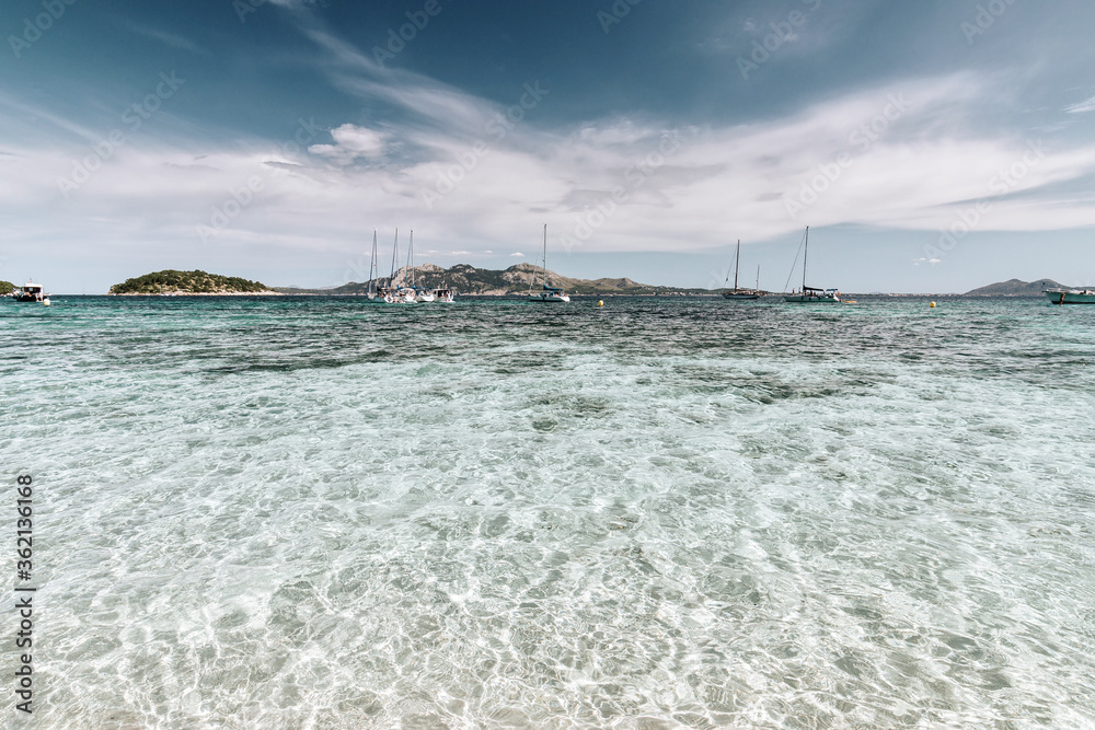 Beautiful cristal clear water scene in Formentor beach Majorca, seascape with an island coast and sailboats on the horizon.