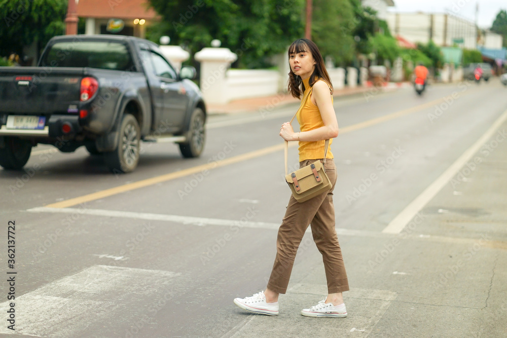 full length of young Asian traveling woman waiting for traffic lights to cross local road in Nan, Thailand