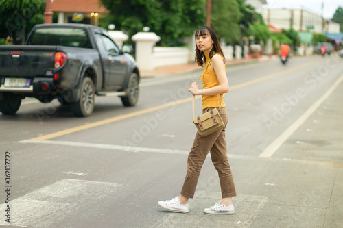 full length of young Asian traveling woman waiting for traffic lights to cross local road in Nan, Thailand