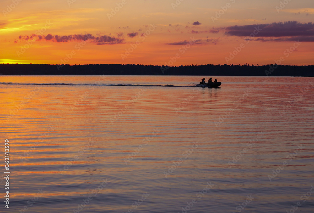 Fototapeta premium People vacationing in nature or fishermen go by boat on the lake during a beautiful sunset.