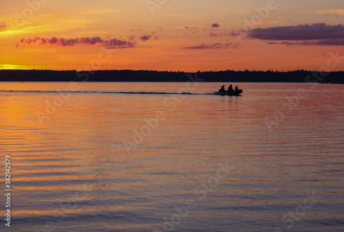 Billede på lærred People vacationing in nature or fishermen go by boat on the lake during a beautiful sunset