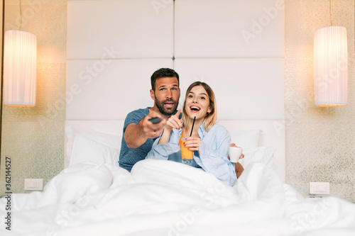 Couple drinking coffee and orange juice while watching TV in a hotel room