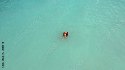Aerial view of young beautiful woman in red bikini and sunglasses in light blue azure turquoise water of sea, relaxing in ocean. Summer beach vacation. Malibu lifeguard. Maldives. Melasti beach Bali
