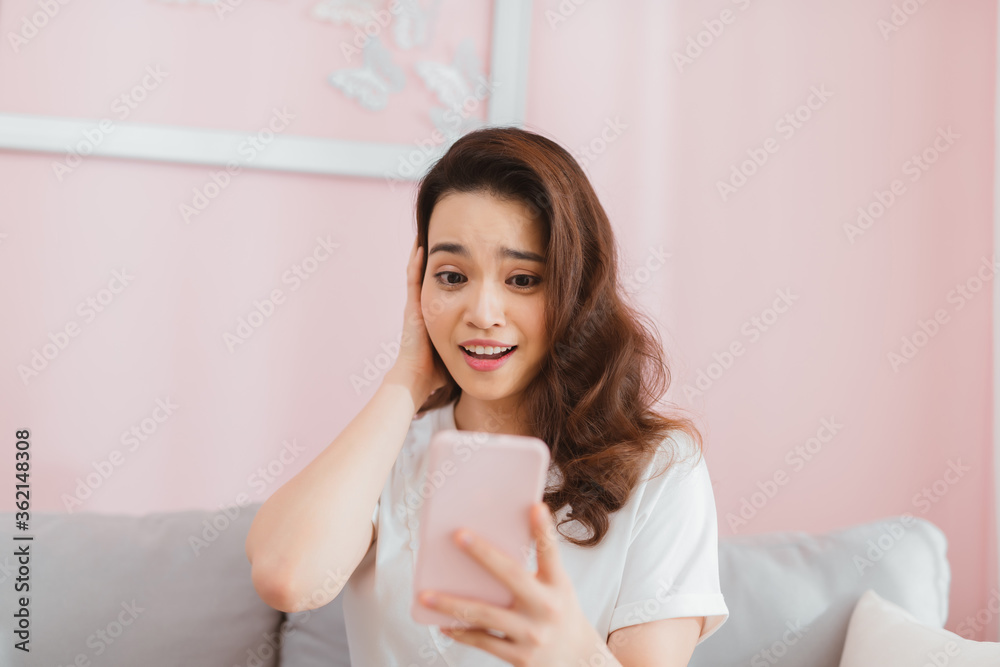 surprised shocked woman looking at phone screen sitting on a sofa in apartment at home surprised shocked woman looking at phone screen sitting on a sofa in apartment at home