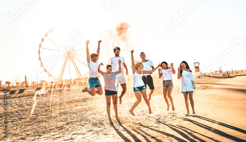 Happy friends group having fun at ferris wheel seaside - Summer vacations friendship concept with millenial guys and girls cheering at public beach - Warm sunset color tone with contrast filtered look photo