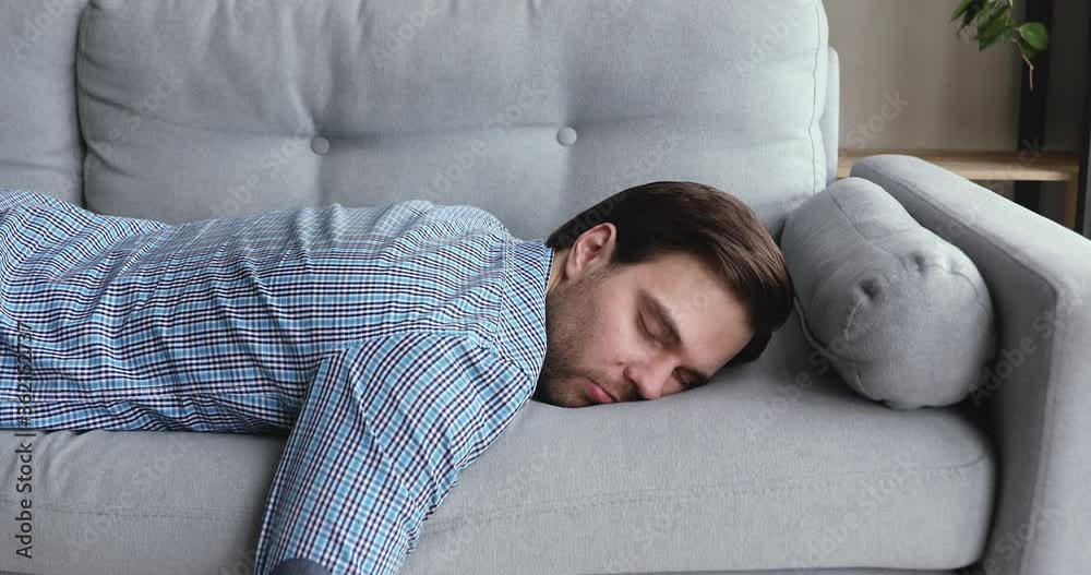 Exhausted overloaded young man in casual shirt came home after work flopped down on sofa feels like squeezed lemon. Concept of after party, tired overworked person hard day, lack of energy, breakdown