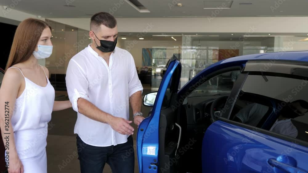Couple in a car salon. European couple in protective masks buying the car during the quarantine Couple in a car salon. European couple in protective masks buying the car during the quarantine