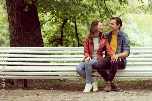 Young, happy, loving couple having date on the bench in the park. Relations, friendship and love.