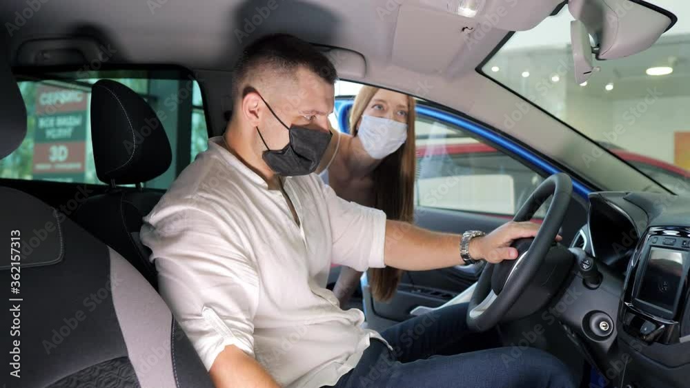 Couple in a car salon. European couple in protective masks buying the car during the quarantine Couple in a car salon. European couple in protective masks buying the car during the quarantine