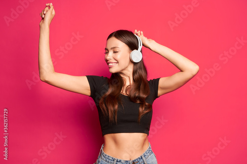 Girl smiling in headphones dances and listens to music on a pink background © Антон Пухов