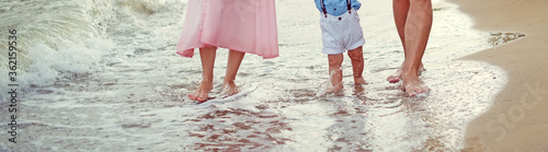 Family Father mother and little son walk barefoot along the seashore on the wet sand at the water's edge cropped. Summer family holidays, vacation concept