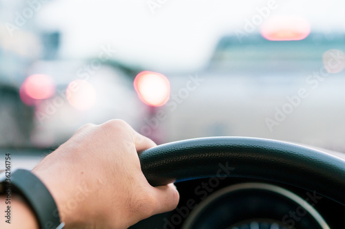 Driver holding a steering wheel on the top (12 O'Clock position) while driving a car on heavy traffic road. Asian driver driving a vehicle on highway close up.
