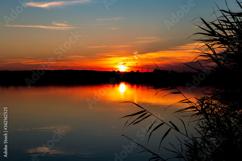 Bright beautiful red orange sunset with reflection in the evening over the horizon above the water on the shore of the pond, fishing, outdoor activities, tourism, nature of Russia in Saratov region © Светлана Евграфова