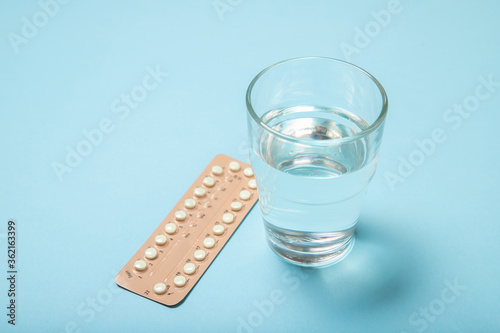 Female oral contraceptives and a glass of water on a blue background