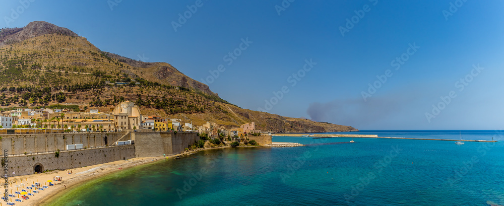 The beach, impressive seawall and mountain backdrop of Castellammare del Golfo, Sicily in the summertime