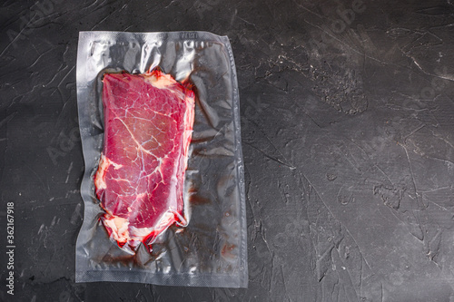 Rump beef steak for sous vide cooking on black stone background, top view space for text.