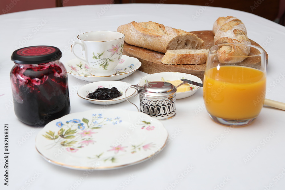 baguette, a cup of tea, orange juice, jam on a white table baguette, a cup of tea, orange juice, jam on a white table