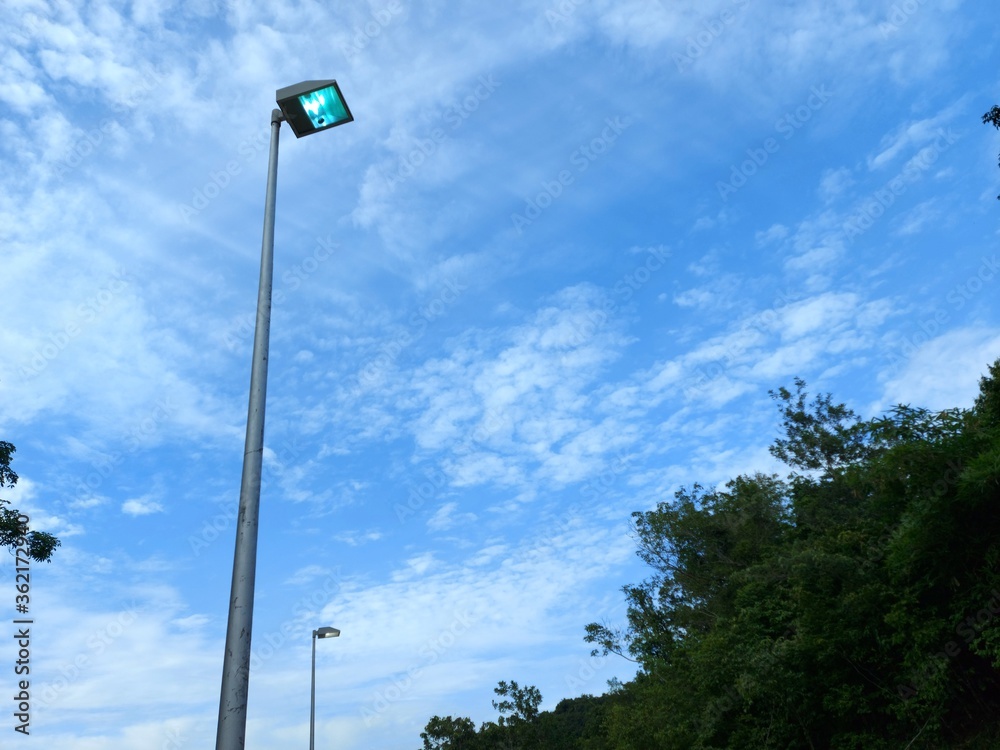 Street lamp post, with green trees and blue skies as the background