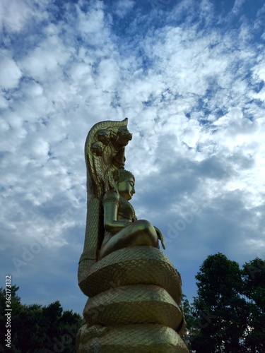 Golden Buddha statue on a pedestal, background of trees and sky.