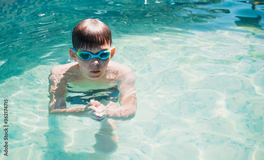 Boy in swimming glasses swims in the pool. Swimming in the pool. Summer activities.