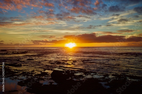 Surfing in Atlantic ocean in bright colorful sunset lights. Majestic colorful sunset on Atlantic ocean coast. Beautiful sunset on Tenerife island. Panoramic Scenic golden sunset view. Backgrounds. 