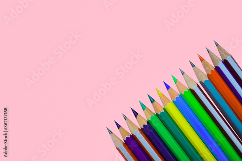 Row of different colored wood pencil crayon placed on a pink color paper