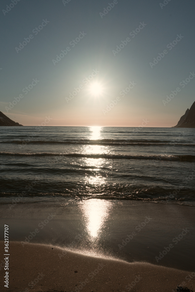 White nights - sunset during the polar day in northern Norway. Long reflections of the sun in the water observing from the sandy beach.