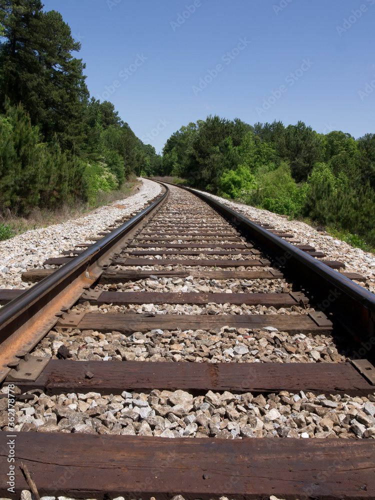 Single line railroad spur track making a gradual curve fading into a forested area