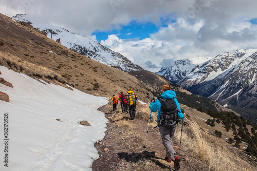 A group of Climbers Hiking high in the mountains in sunny day. Hiking trail among Snow-covered white mountain peaks. Sport in the Mountains. People climbing to the top of the snowy mountain. 