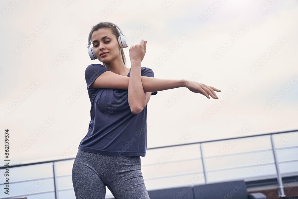 Charming young woman in headphones doing exercise outdoors Charming young woman in headphones doing exercise outdoors