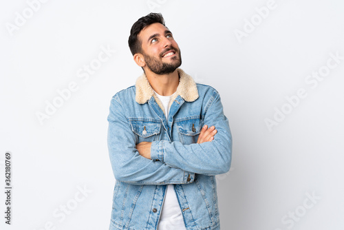 Young handsome man with beard isolated on white background looking up while smiling