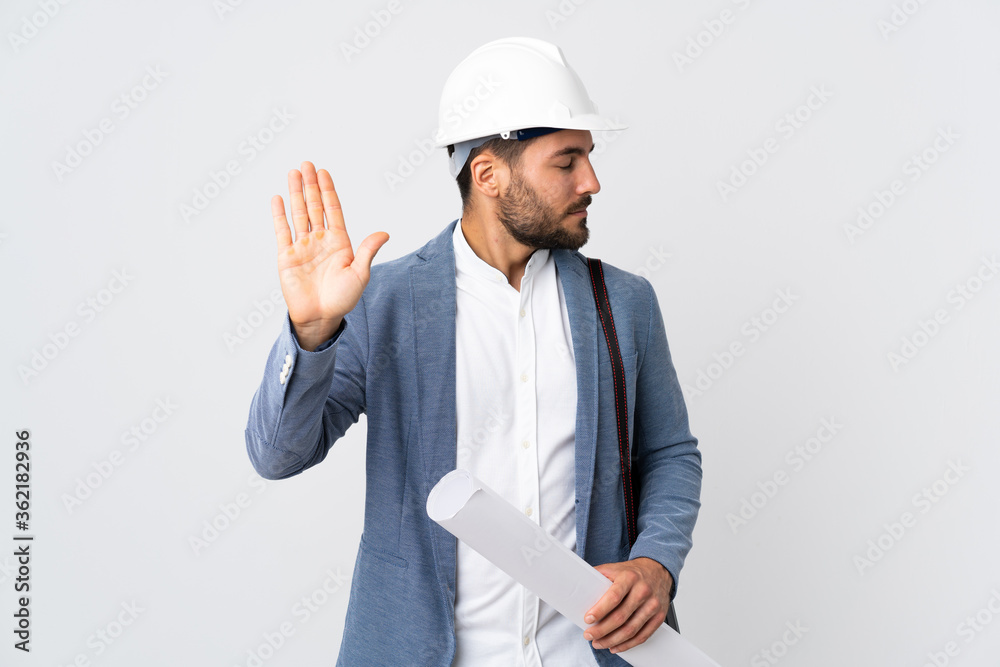 Young architect man with helmet and holding blueprints isolated on white background making stop gesture and disappointed Young architect man with helmet and holding blueprints isolated on white background making stop gesture and disappointed