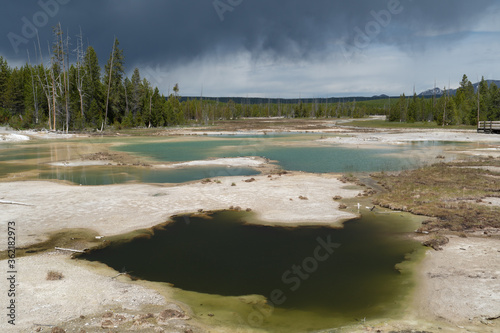 Hydrothermal 10 pools causing rising stream and bubbling water extracting minerals from the ground in various colors of green, gray and orange with views of distance mountains, Norris Porcelain Basin