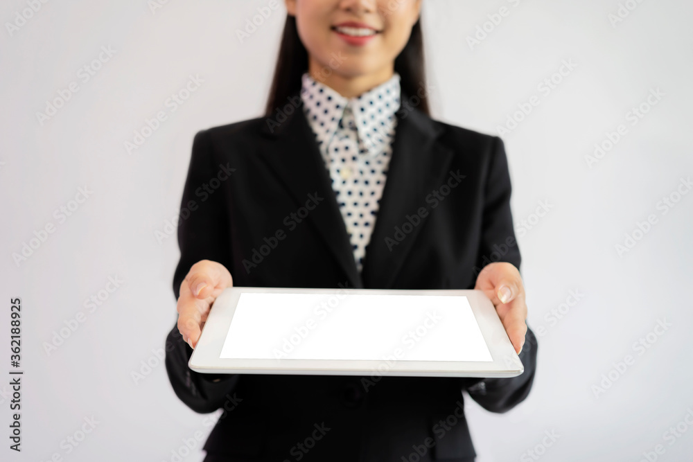 Portrait of an Asian businesswoman wearing a black suit. Hold an empty tablet to put text, images. Gray isolated background Portrait of an Asian businesswoman wearing a black suit. Hold an empty tablet to put text, images. Gray isolated background