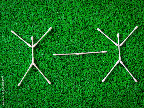 Top view of cotton ear sticks arranged as two human beings with white line represent social distance of coronavirus or covid-19 issue. Social distancing concept. Green background
