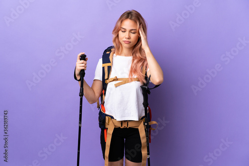 Teenager girl with backpack and trekking poles over isolated purple background with headache
