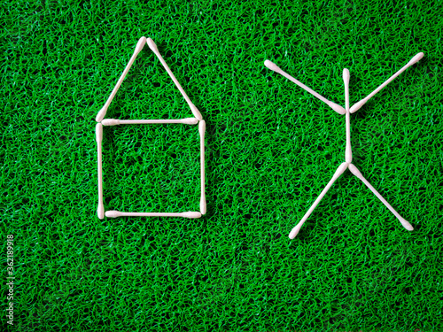 Cotton ear sticks arranged as a little house and as a human being on green background.
