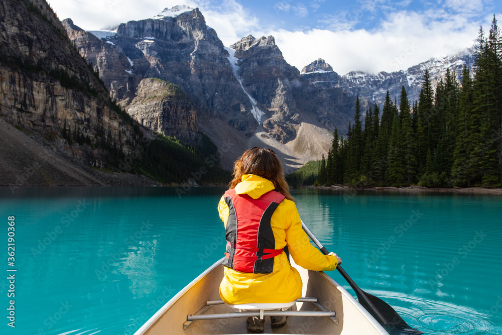 Girl kayaking on a turquoise lake with a yellow rain jacket in the mountains