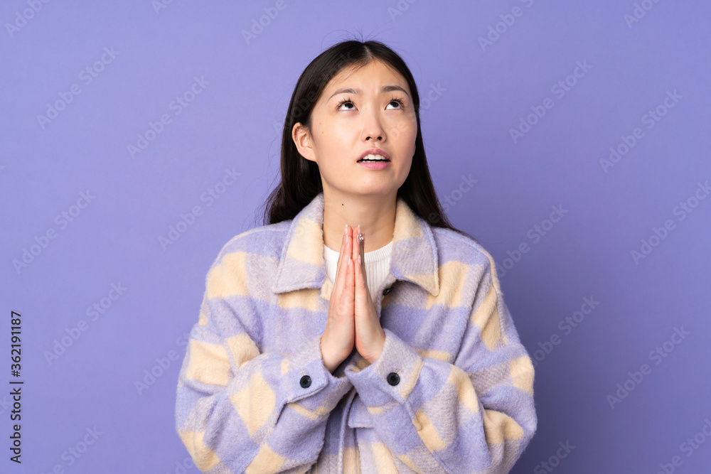 Young asian woman isolated on purple background keeps palm together. Person asks for something Young asian woman isolated on purple background keeps palm together. Person asks for something