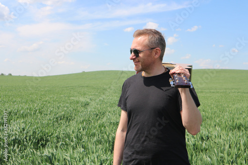 A man in black sunglasses is standing in a field with a guitar on a guitar. Happy guitar player in nature.