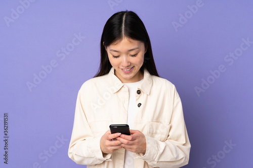 Young asian woman isolated on purple background sending a message with the mobile