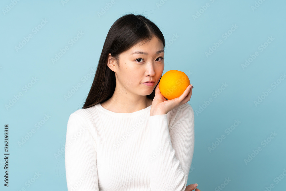 Young asian woman holding an orange over isolated blue background Young asian woman holding an orange over isolated blue background