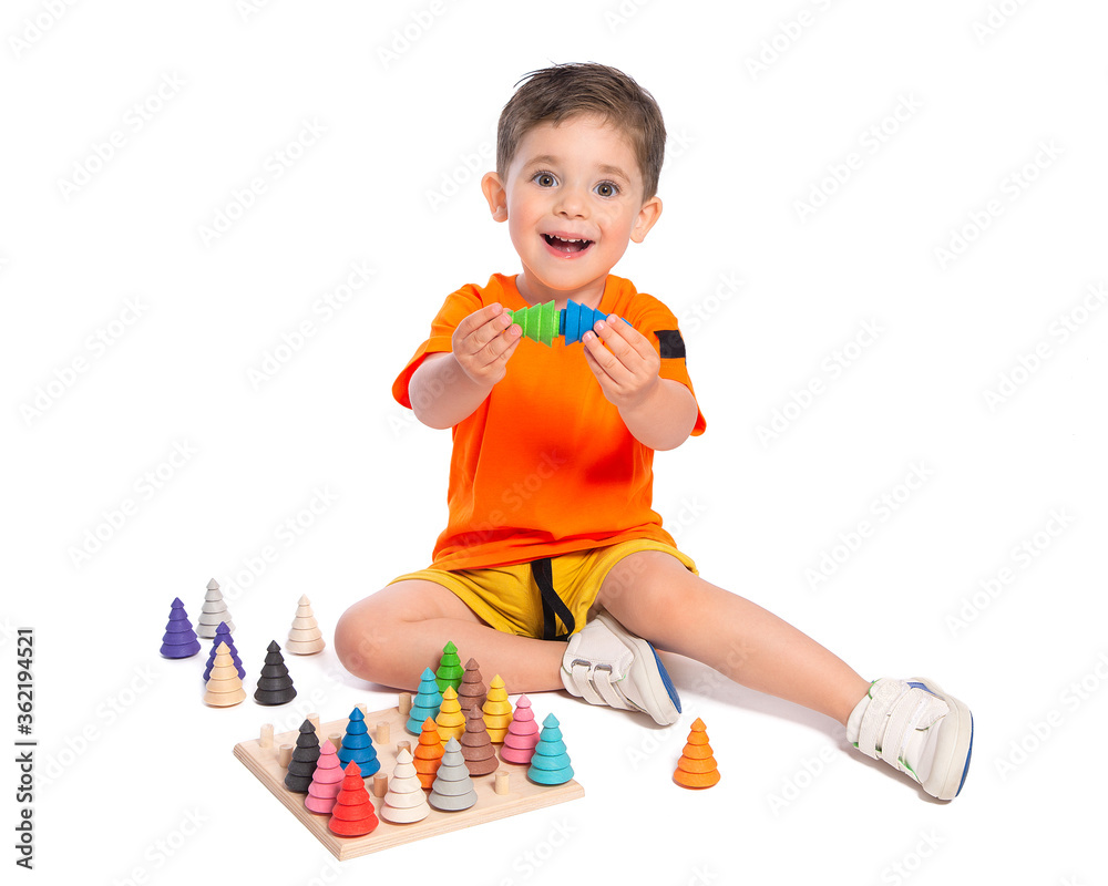 A beautiful European boy plays with wooden Montessori toys on a white