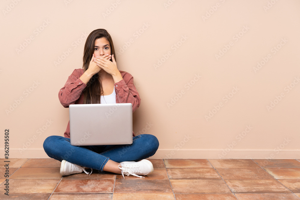 Teenager student girl sitting on the floor with a laptop covering mouth with hands Teenager student girl sitting on the floor with a laptop covering mouth with hands