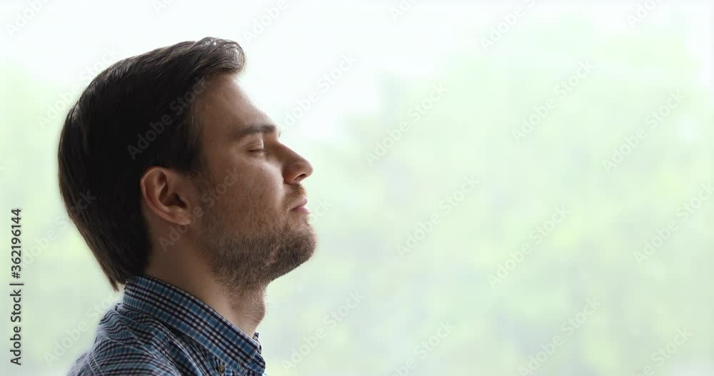 Peaceful man pose aside near window background closed eyes breath fresh air feels calm. Anxiety relief, brings internal state in order exercise, close up side view face. No stress, mindfulness concept Peaceful man pose aside near window background closed eyes breath fresh air feels calm. Anxiety relief, brings internal state in order exercise, close up side view face. No stress, mindfulness concept